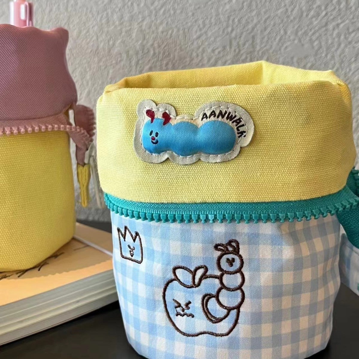 Simple Vertical Flip large capacity pencil case with pastel yellow top and blue checkered bottom featuring cartoon worm and apple embroidery