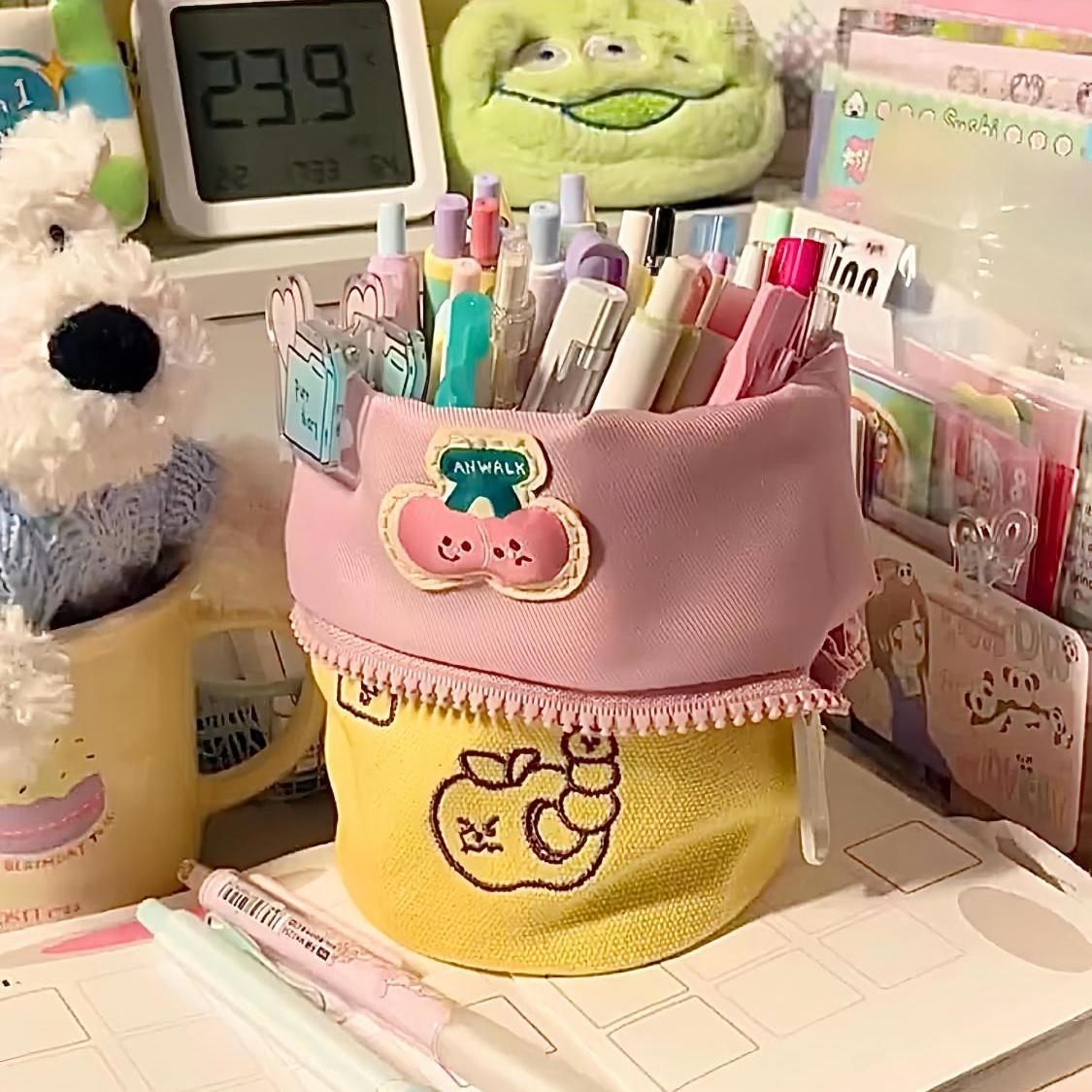 Simple vertical flip large capacity pencil case in pink and yellow holding colorful pens on desk with plush toys and stationery items