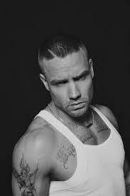 Black and white portrait of Liam Payne in a sleeveless shirt showing tattoos and serious expression